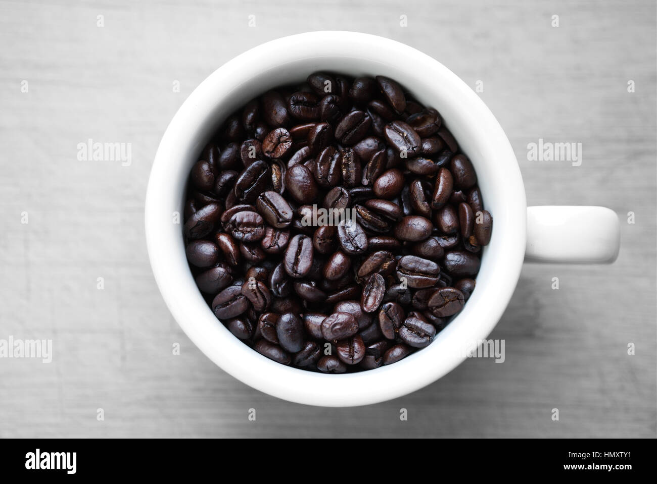 A china coffee cup filled to the brim with Dark Roasted 100% Whole Arabica Coffee Beans Stock Photo