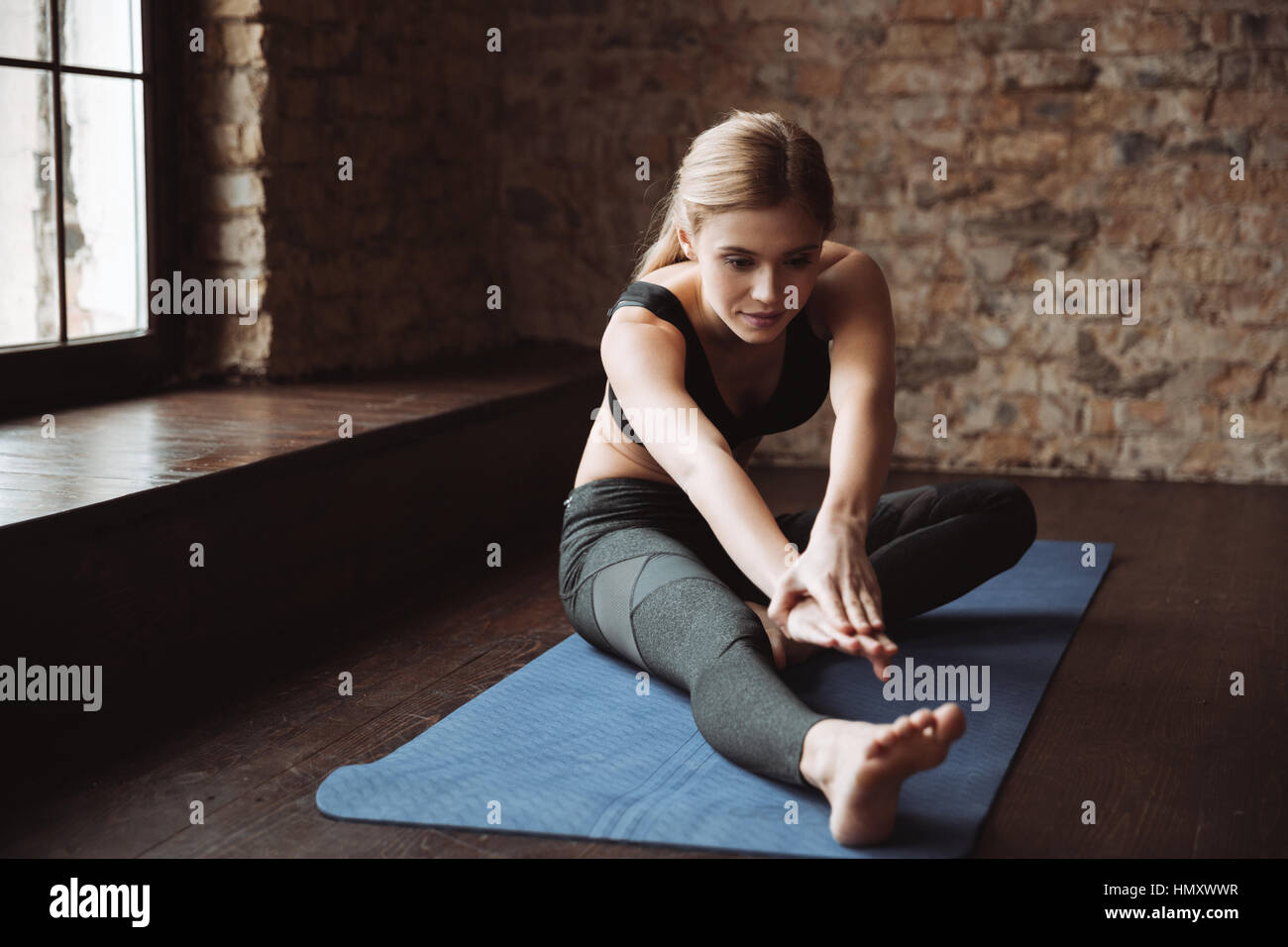 Pretty young fitness woman sitting and stretching her legs on mat Stock ...