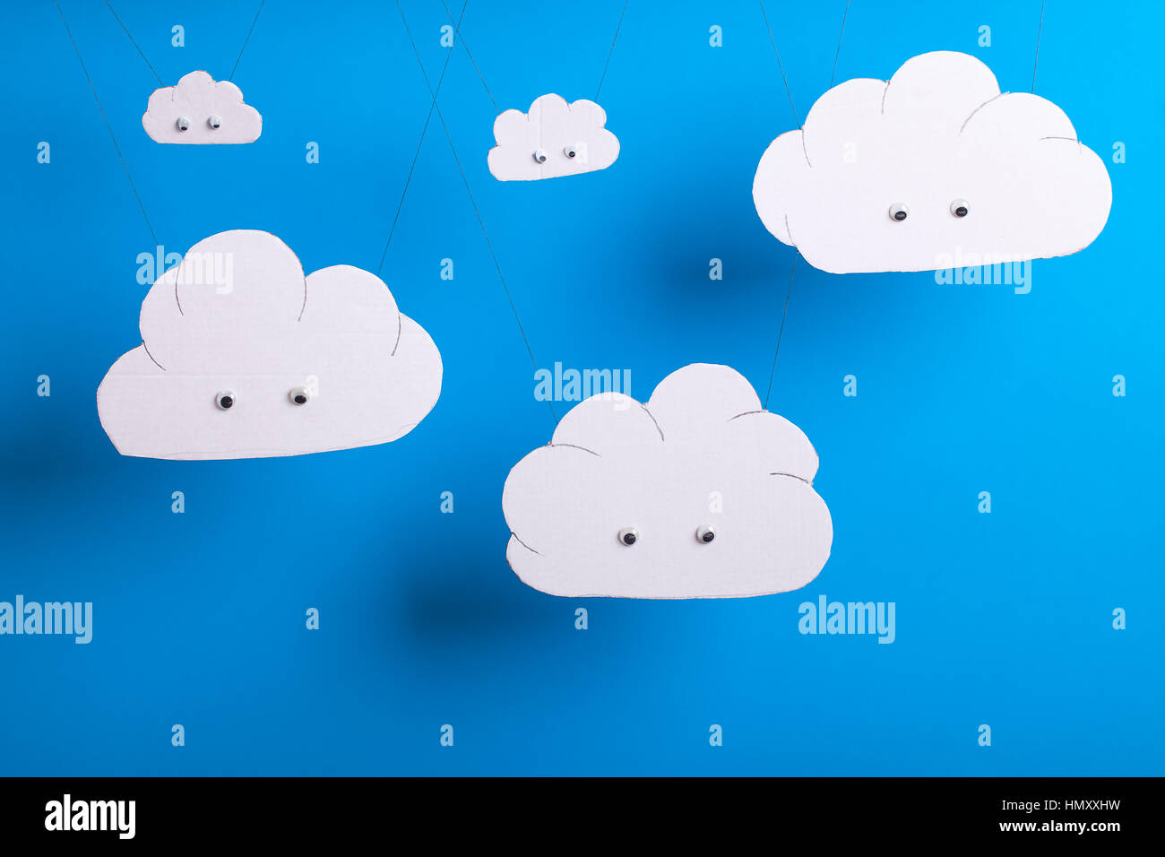 Cloud computing concept with white cardboard cutout cute clouds with eyes hanging in front of a sky blue background. Stock Photo