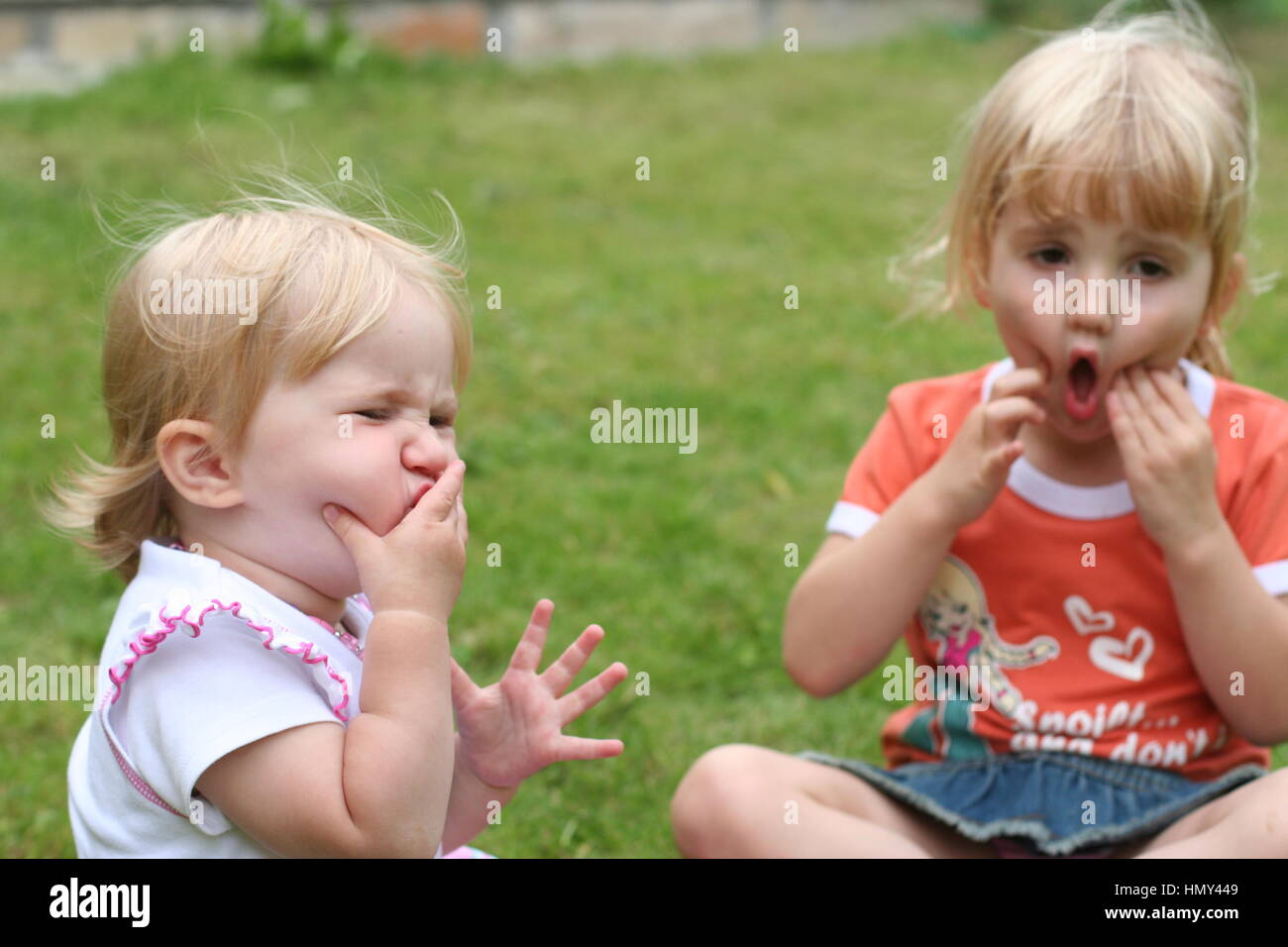 Blonde Children kids, two little girls making faces in the garden Stock Photo