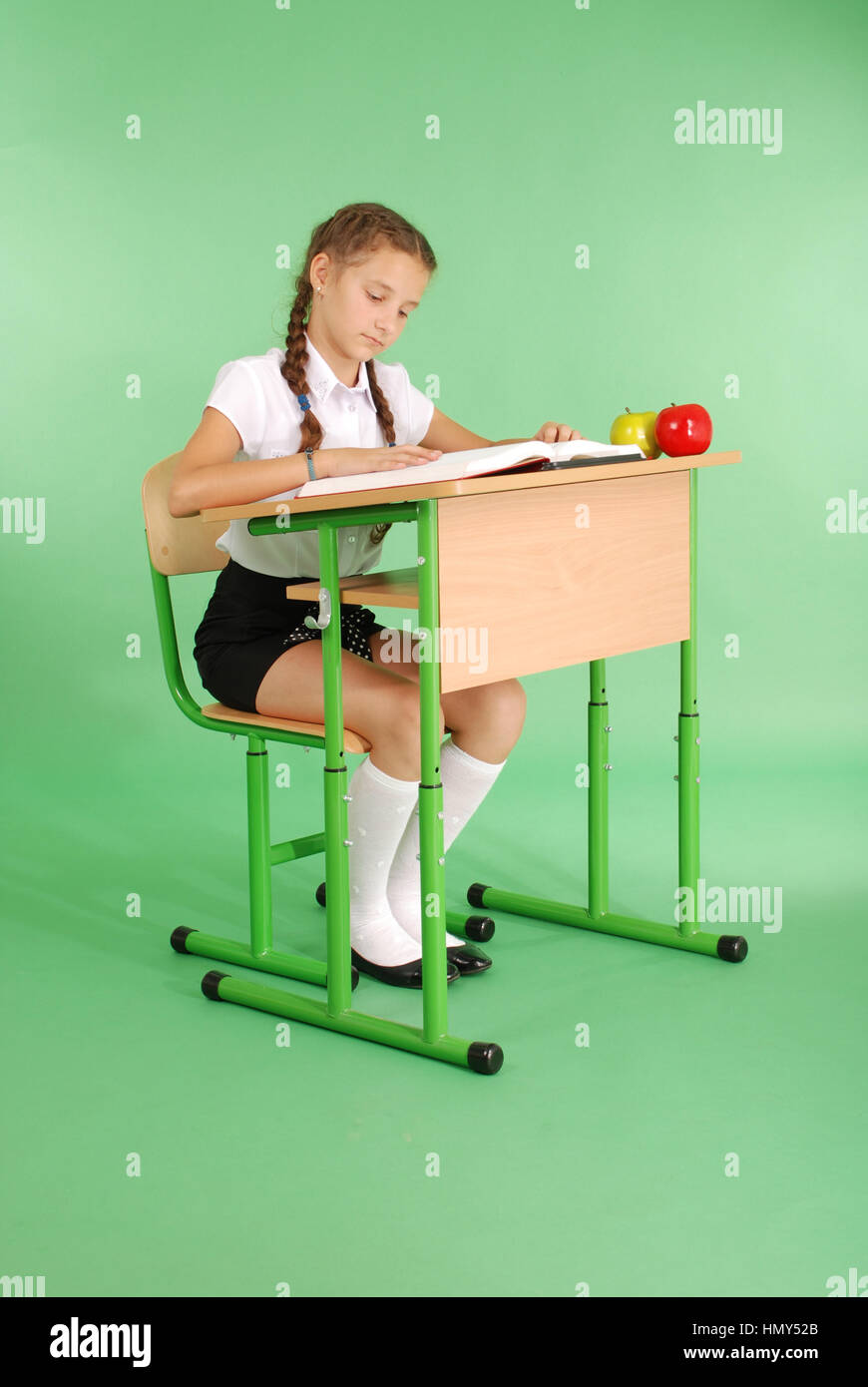 Girl in a school uniform sitting at a desk and reading a book isolated ...