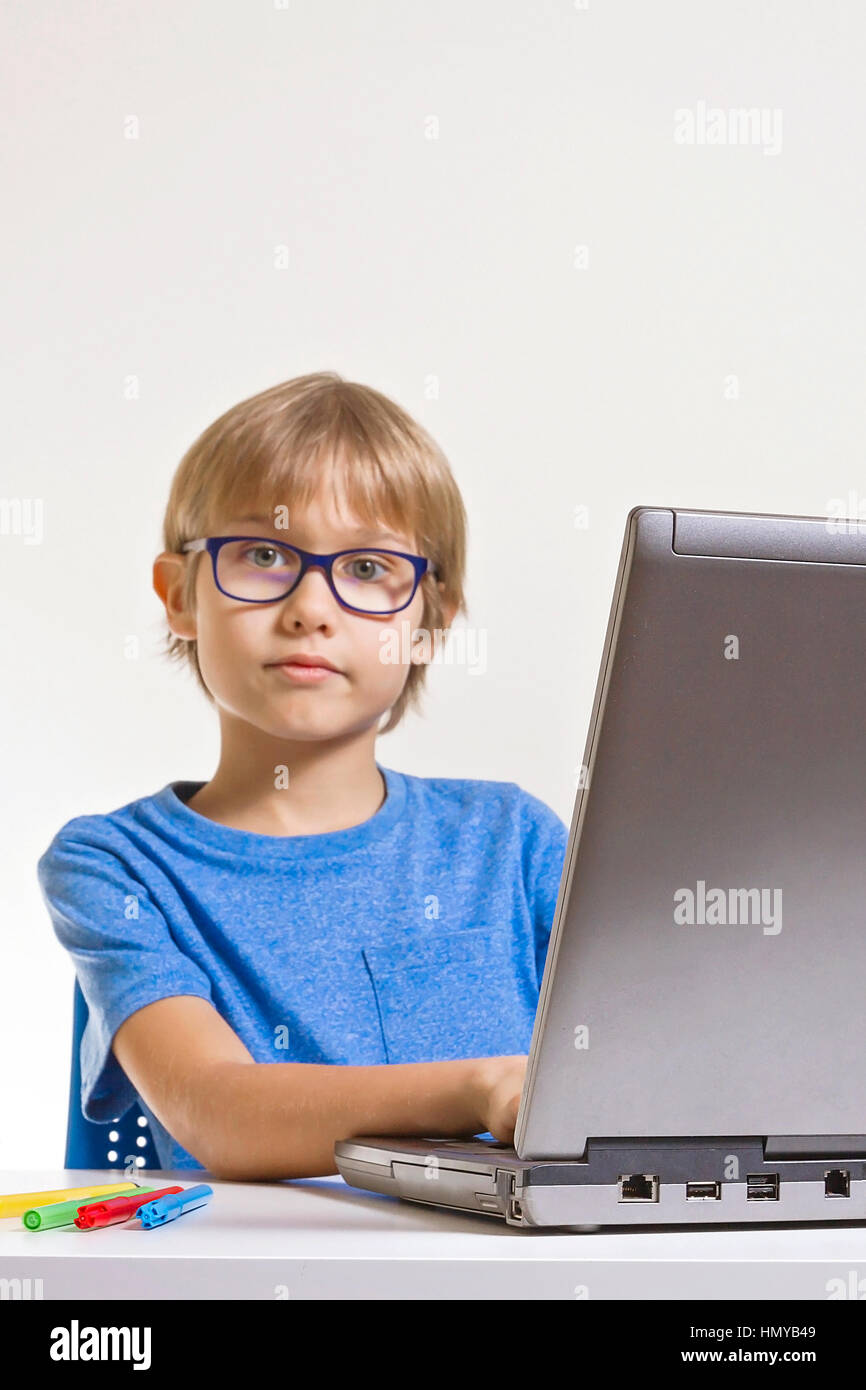 Boy with glasses using laptop computer while sitting on desk at home