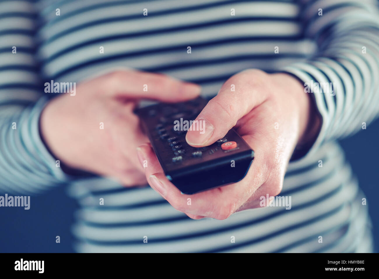 Television remote control in female hands pointing to tv set and turning it on or off Stock Photo