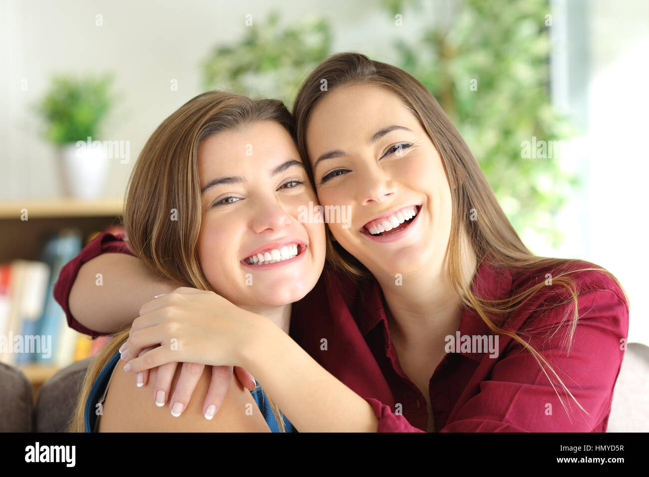 Front view portrait of a two happy friends or sisters posing smiling and looking at you with a homey background Stock Photo