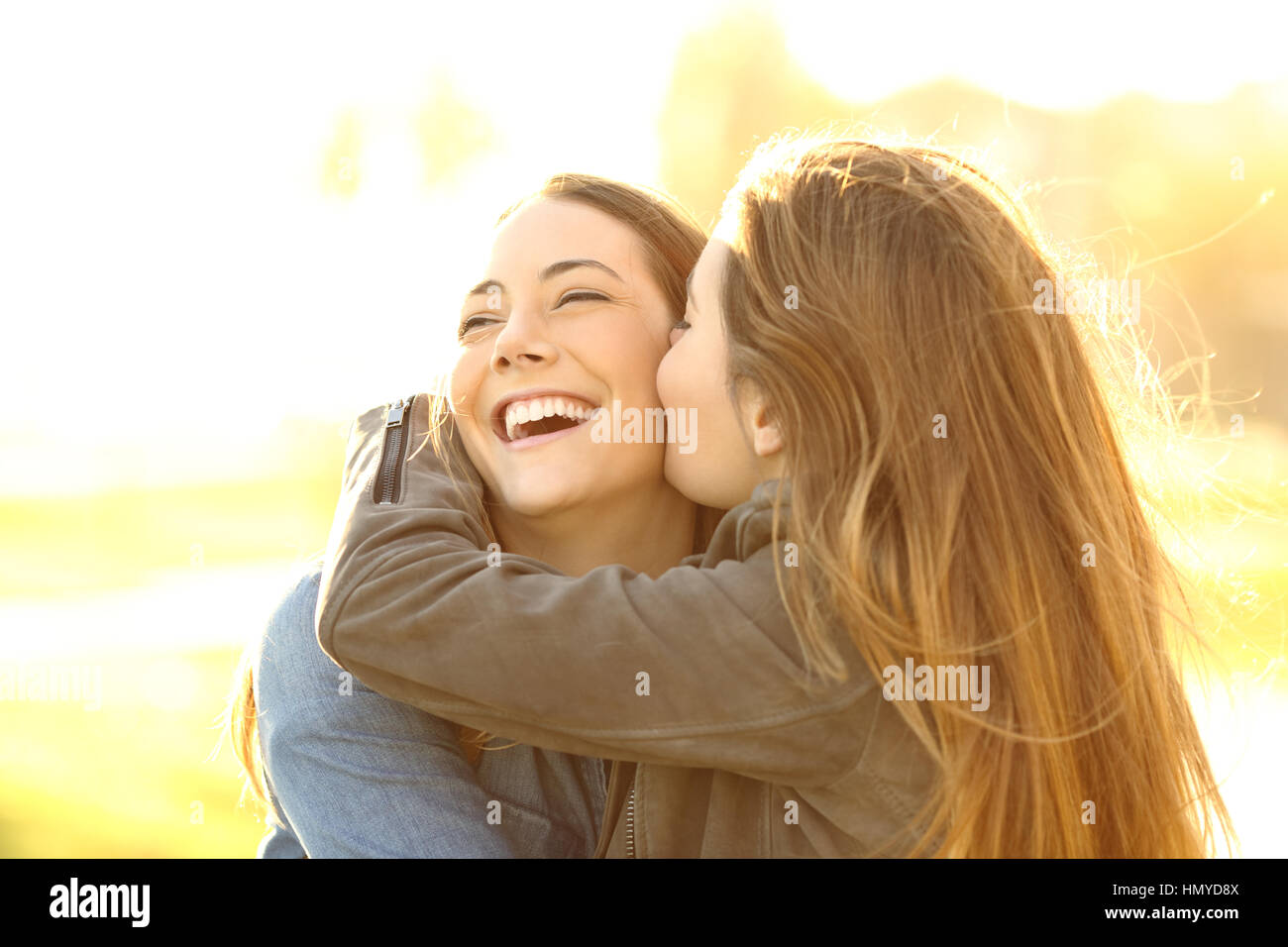 Two happy friends hugging and kissing in the street at sunset with a warm light Stock Photo