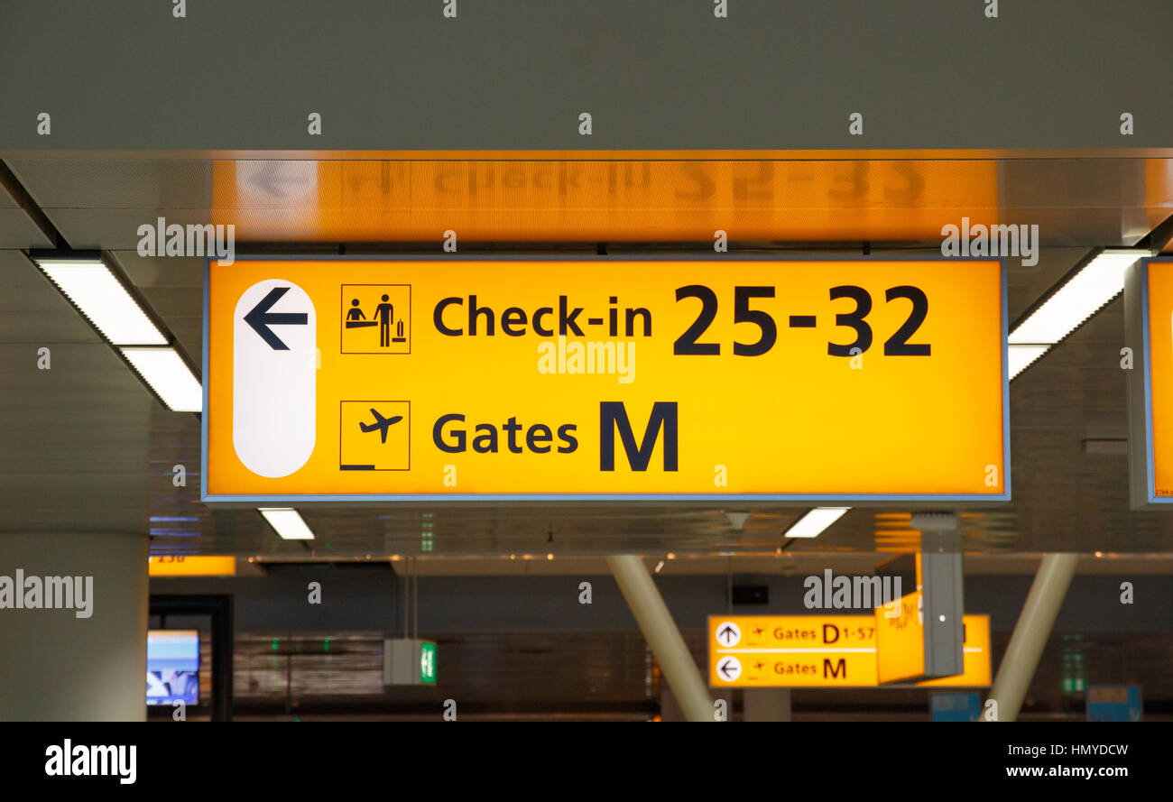 Yellow illuminated sign with gate number and check-in desks Stock Photo