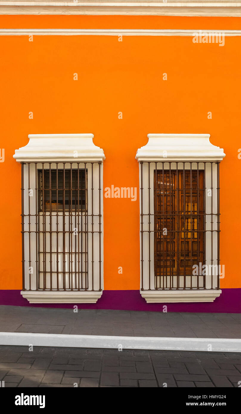 Two windows with bars on orange wall down the street Stock Photo