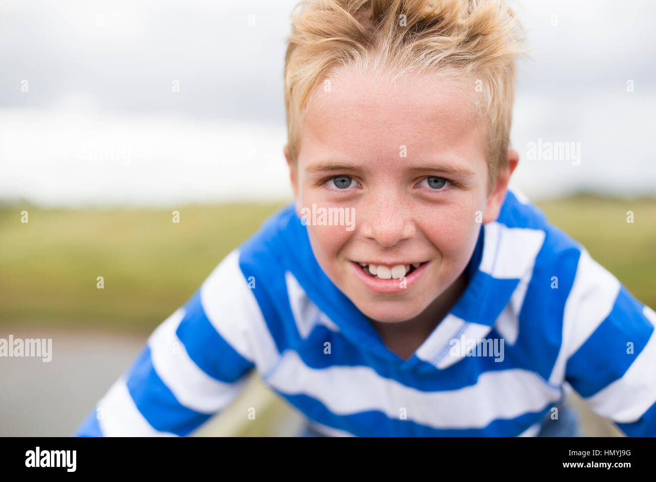 Portrait of a teenage boy smiling at the camera. He is outdoors and wearing casual clothing. Stock Photo