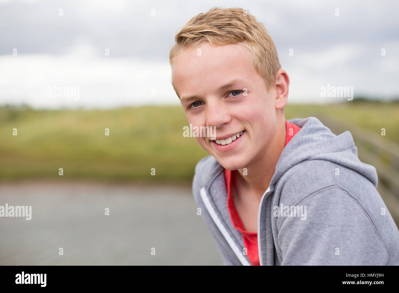 Portrait of a teenage boy smiling at the camera. He is outdoors and wearing casual clothing. Stock Photo