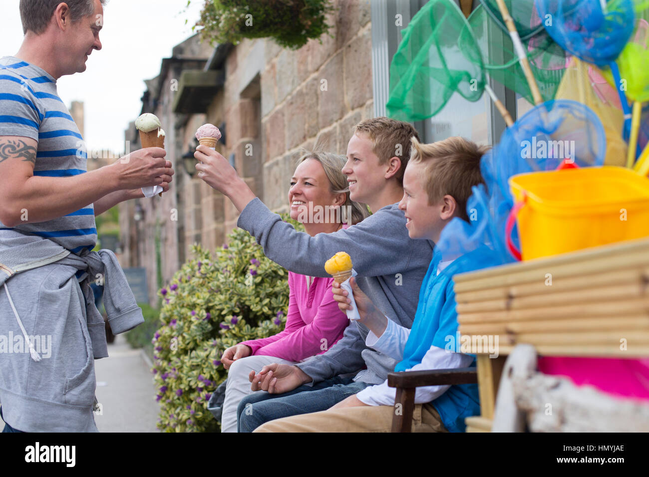 Family enjoying ice cream outside of a shop. They are all holding their cones and smiling. Stock Photo