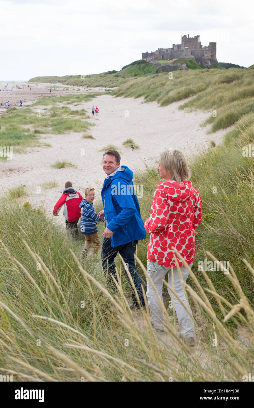 Family of four running down the sandunes onto the beach. A castle can be seen in the background. Stock Photo