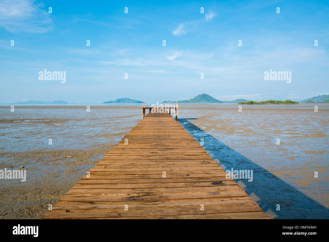 Wood bridge over land extends into the sea during ebb tide time with blue sky background Stock Photo