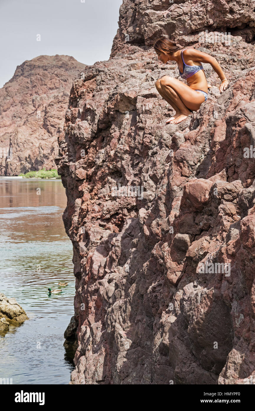 a woman sitting above the Colorado River in a bikini preparing to jump Stock Photo