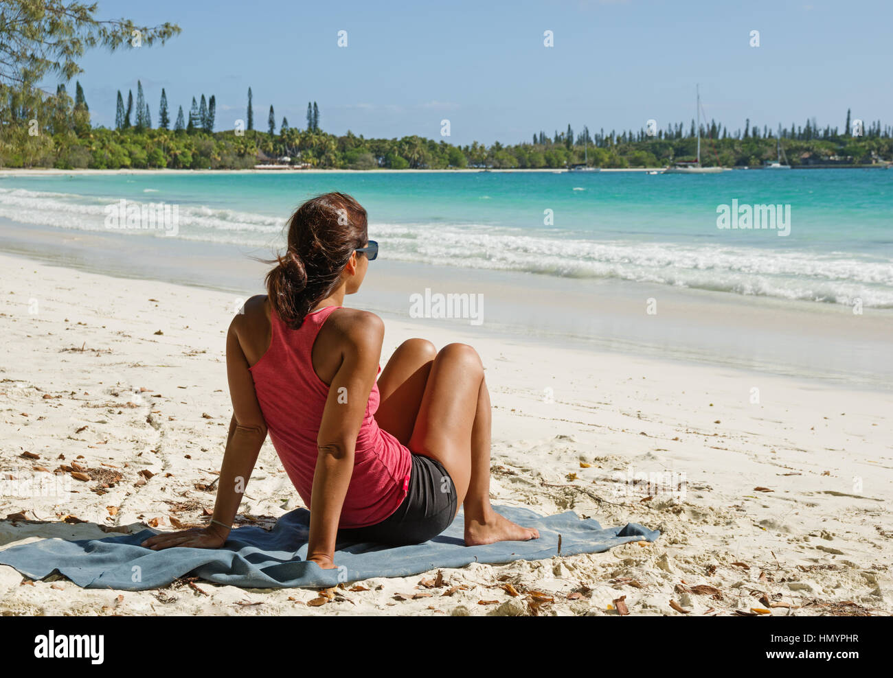 a woman sits on a tropical beach on Isle Of Pines in New Caledonia Stock Photo