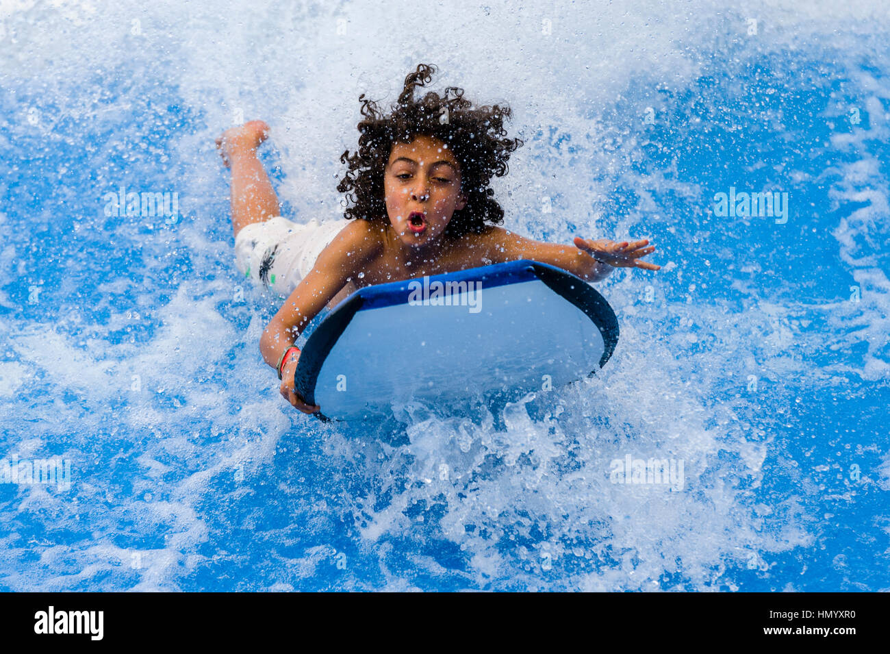 A boy rides a bodyboard on a artificial wave machine at a swimming pool. Stock Photo