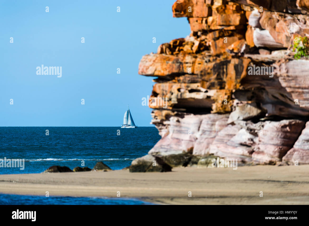 A catamaran sailing past a secluded beach on a desert coastline. Stock Photo