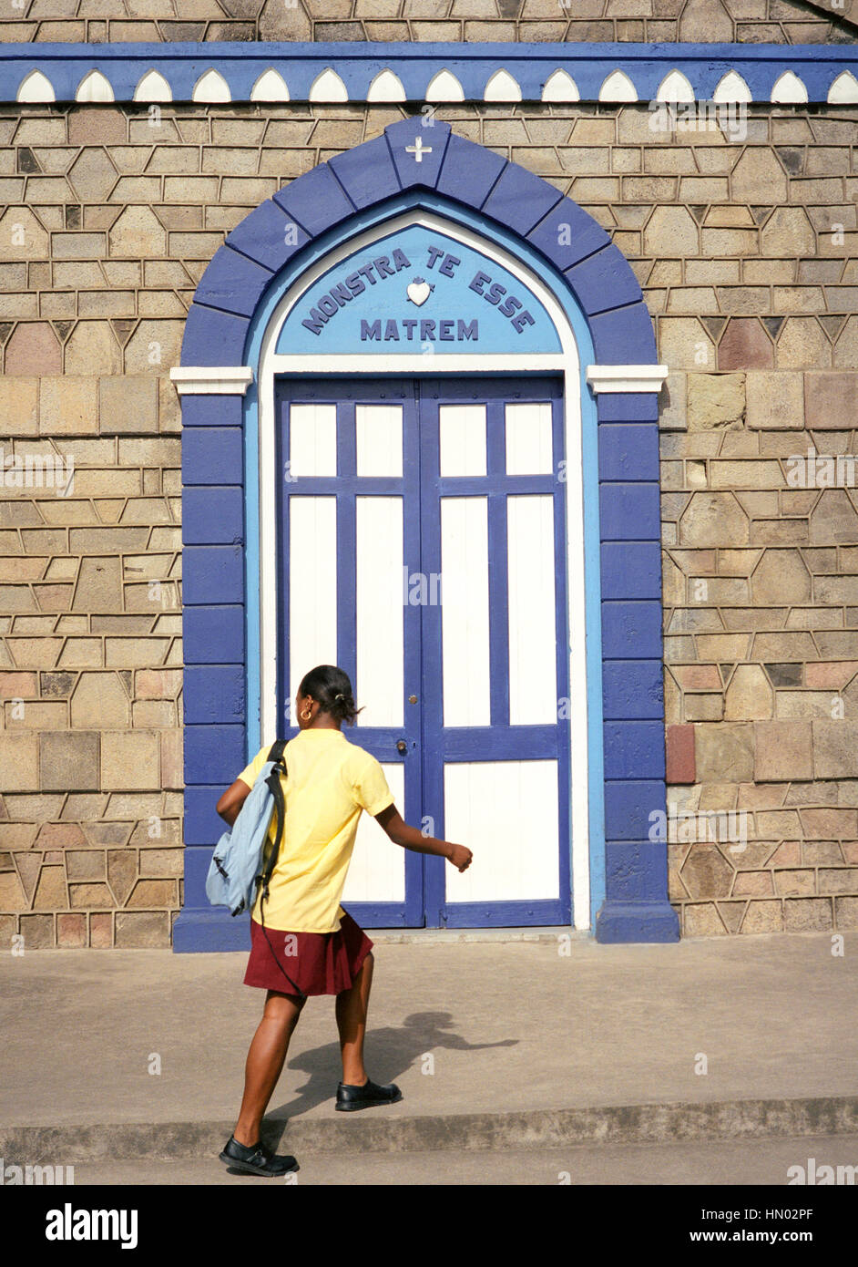 A teenage schoolgirl walks by the Church of the Assumption of the Blessed Virgin Mary on the town square in Soufriere. St. Lucia. Stock Photo