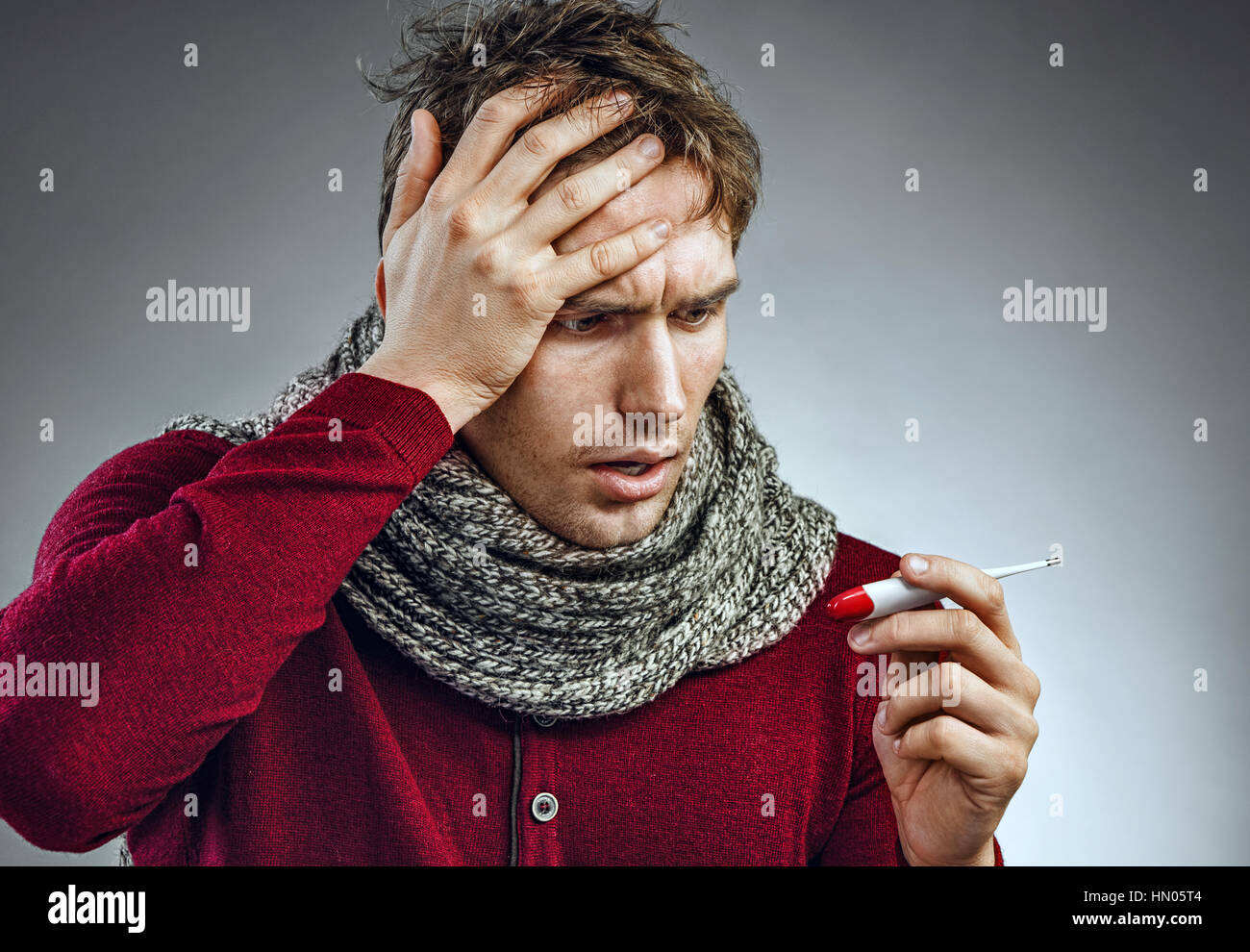 Attractive man reading his temperature on a thermometer. Ill man suffering cold and winter flu virus. Health care concept Stock Photo