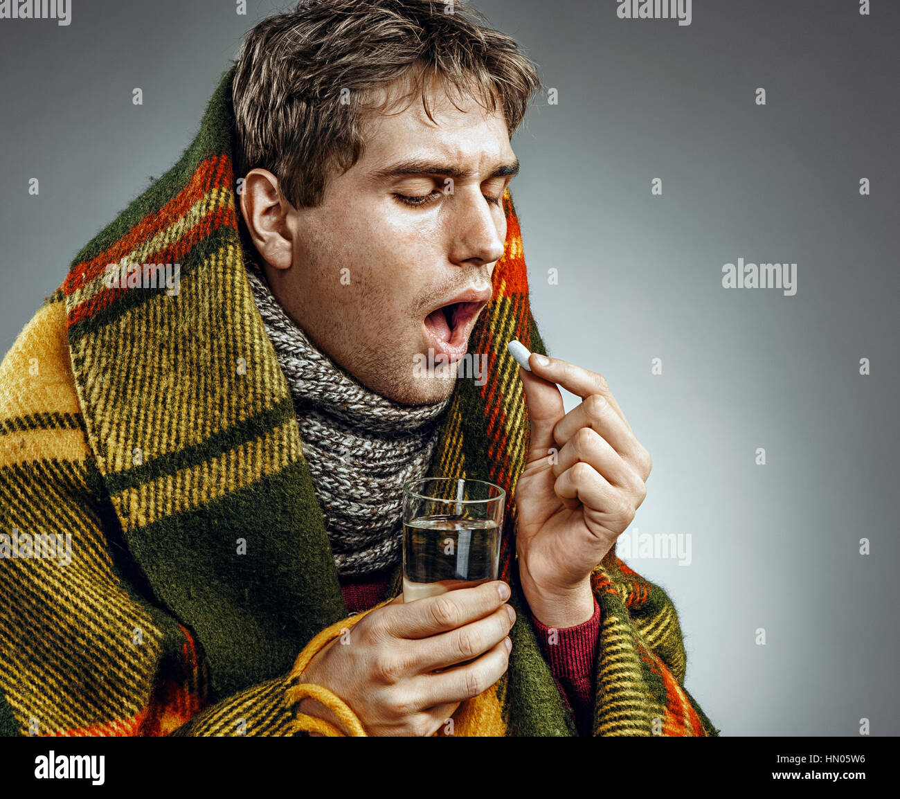 Ill Man covered with plaid blanket take medicine pill with a glass of