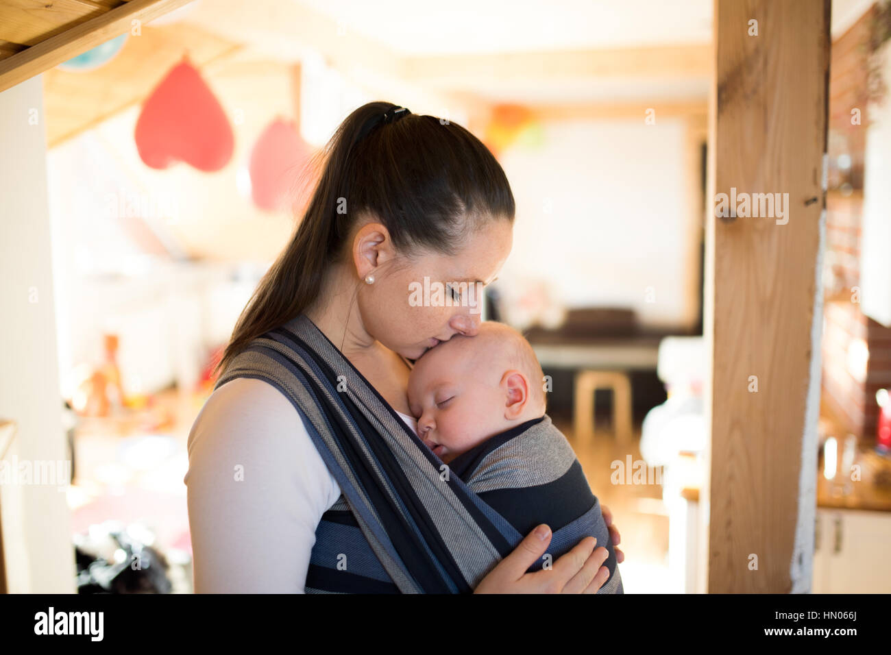 Mother at home with her son in sling, kissing him Stock Photo Alamy