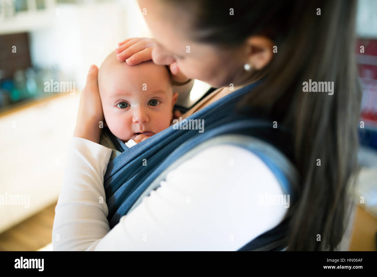 Mother at home with her son in sling, stroking him Stock Photo