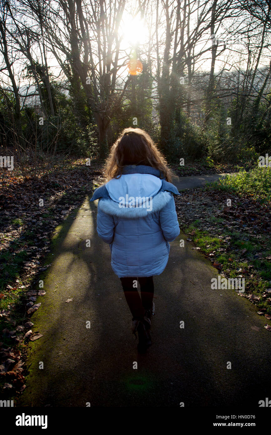 Following a young female walking away through a park. Rear view. Stock Photo