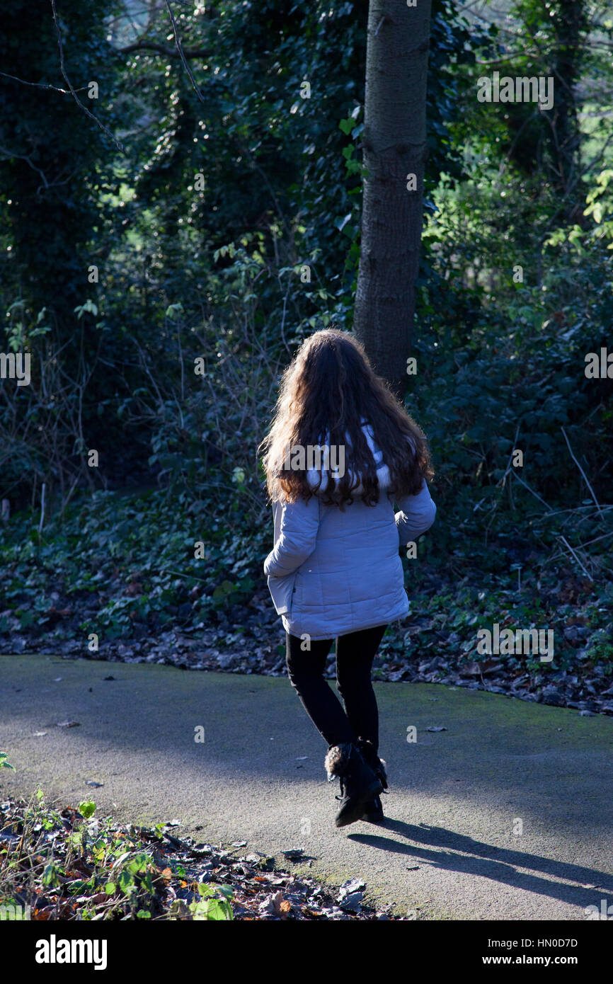 Young female walking away through a park. Rear view. Stock Photo