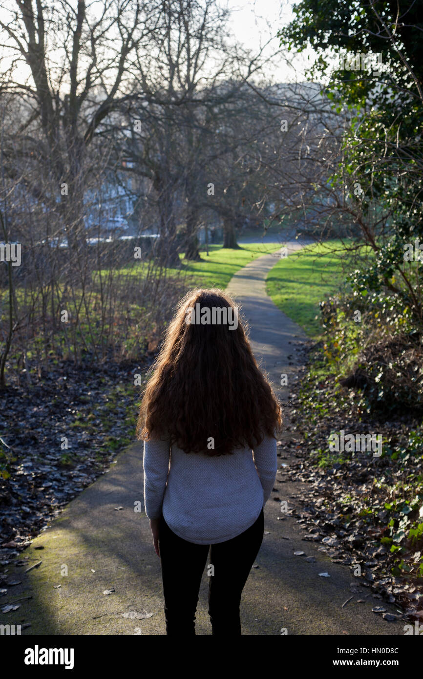 Rear view shot of a young woman walking along a park through a park. Stock Photo