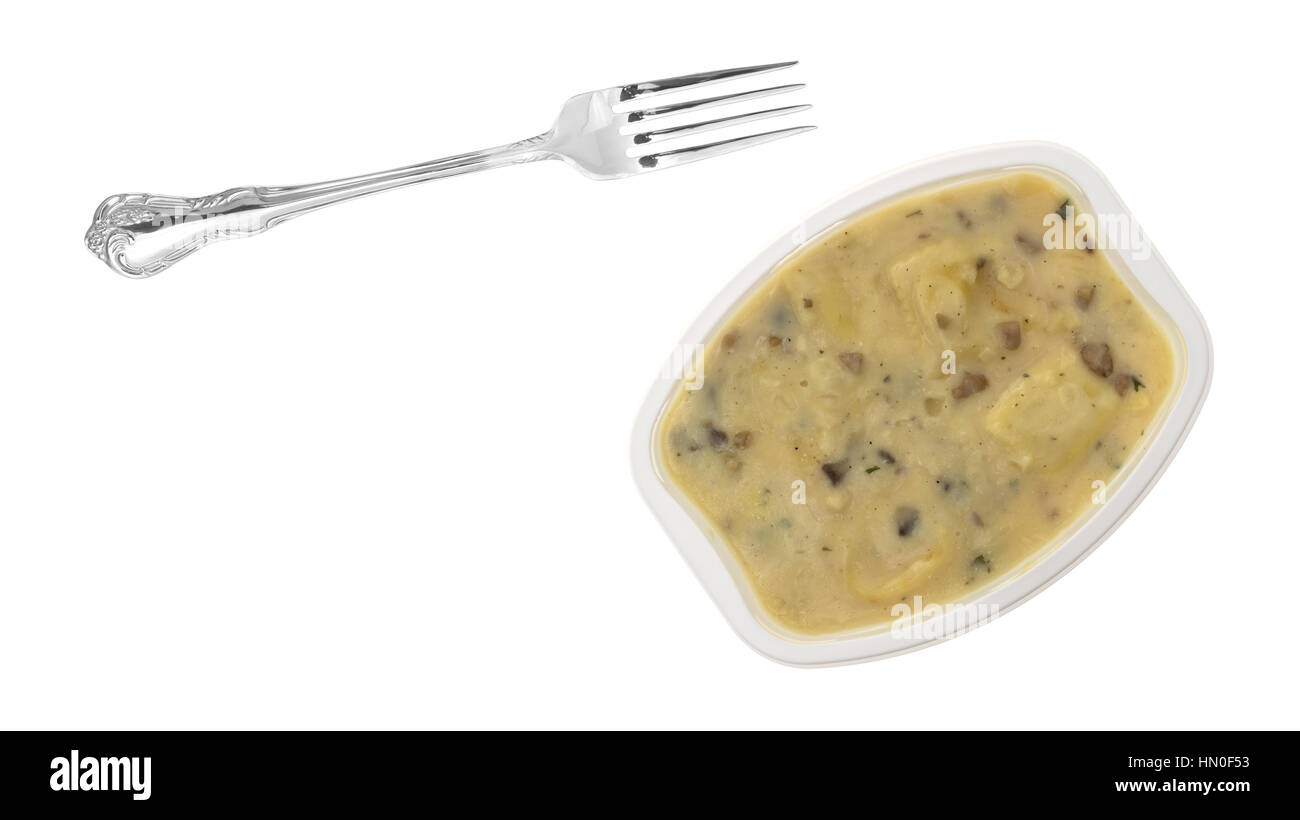 A fork to the side of a ravioli in a cheese and mushroom sauce TV dinner isolated on a white background. Stock Photo