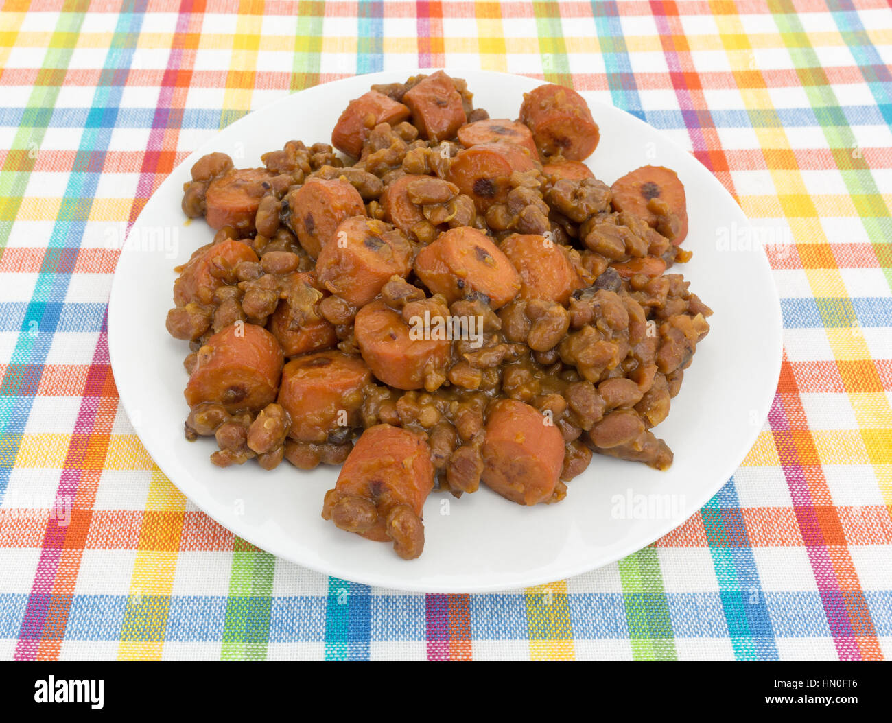 Baked beans and sliced hot dogs on a plate atop a colorful place mat