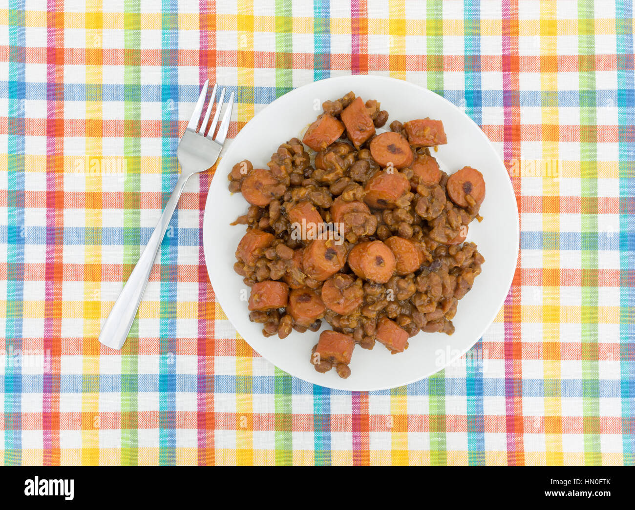 Baked beans and sliced hot dogs on a plate atop a colorful place mat