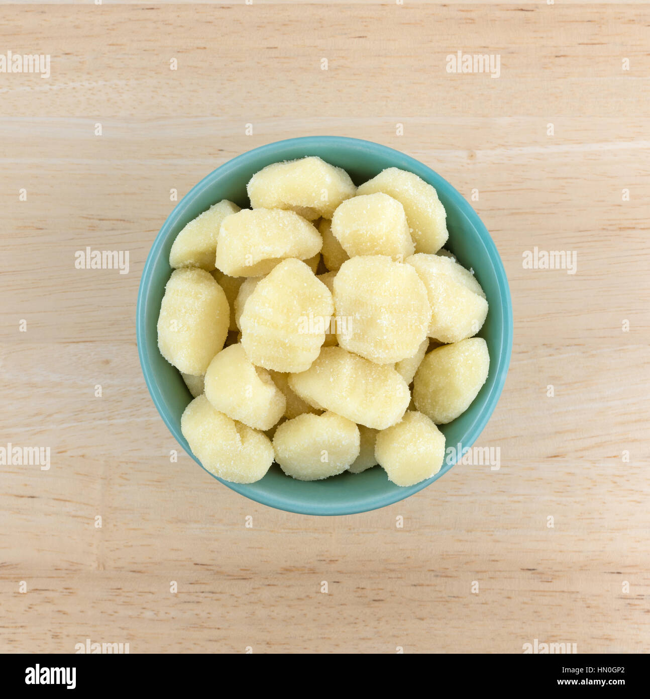 Top view of plain potato gnocchi in a green bowl atop a wood table. Stock Photo