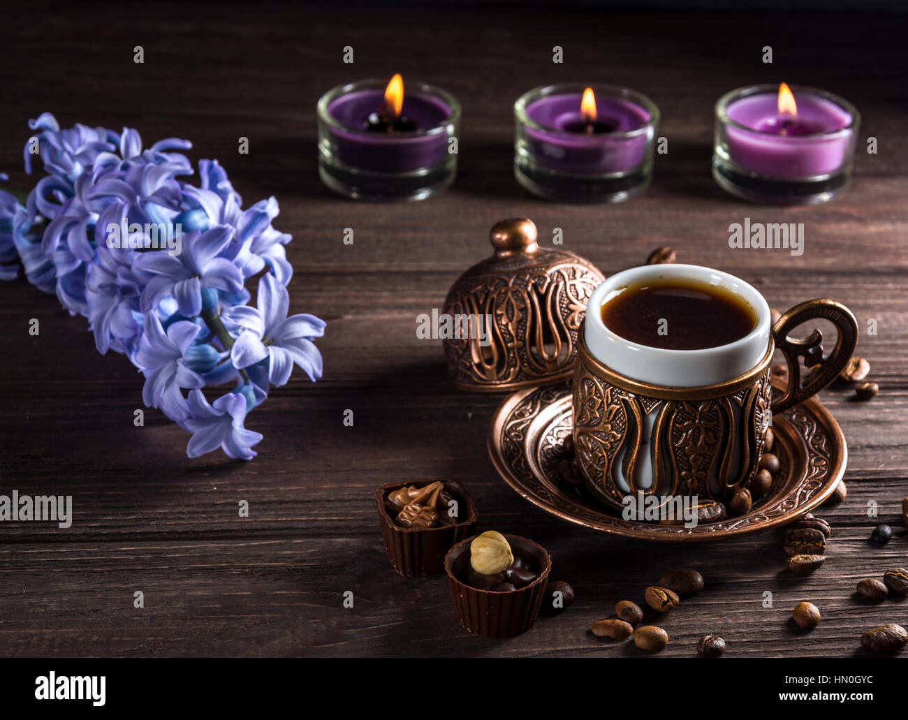 Cup of black coffee, candles and flowers on a wooden background. Dark key. Stock Photo