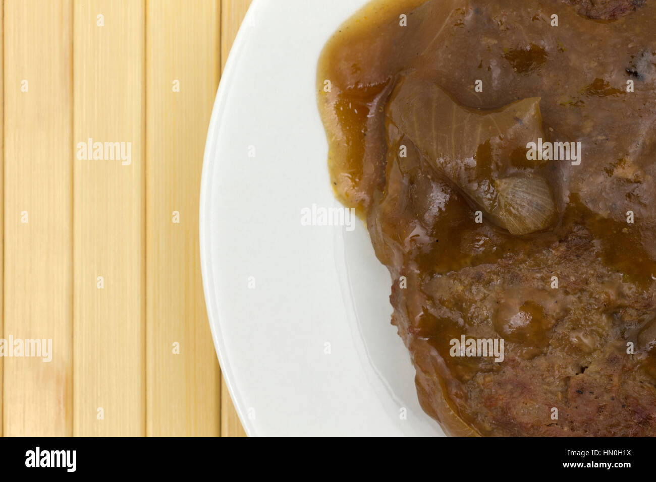 Top close view of salisbury steak with gravy on a plate atop a wood place mat. Stock Photo
