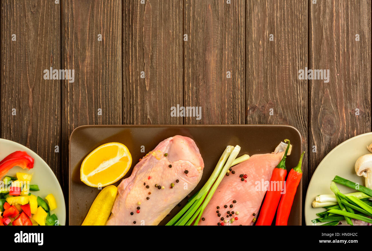 The chicken fillet and vegetables prepared for frying on a brown wooden background. Top view, copy space. Stock Photo