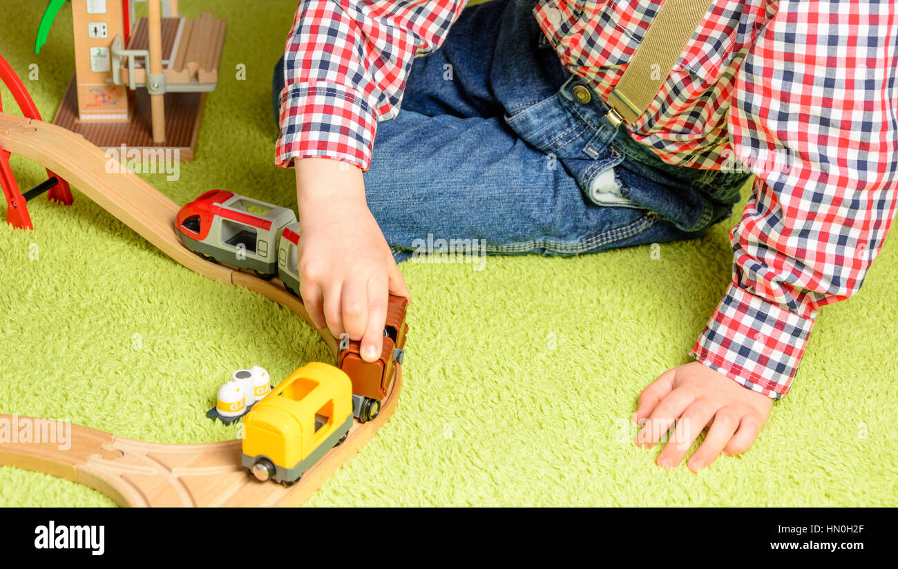 the boy plays the wooden railway sitting on a green carpet Stock Photo