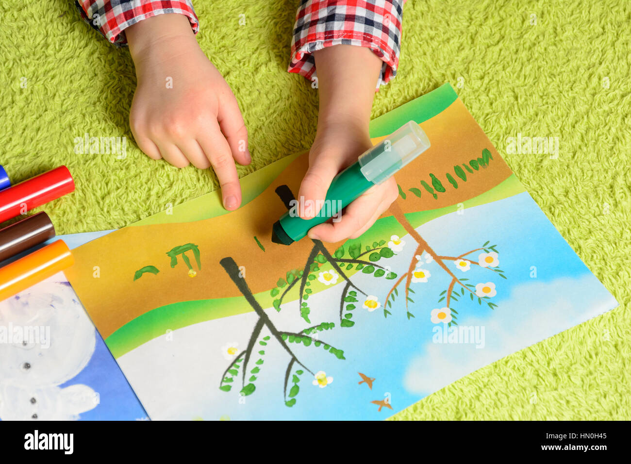 the child draws a picture lying on a green carpet Stock Photo