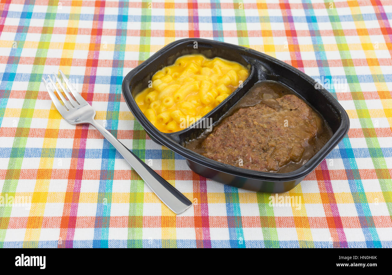 A TV dinner meal of salisbury steak with gravy macaroni and cheese in a black tray with a fork to the side on a colorful place mat. Stock Photo