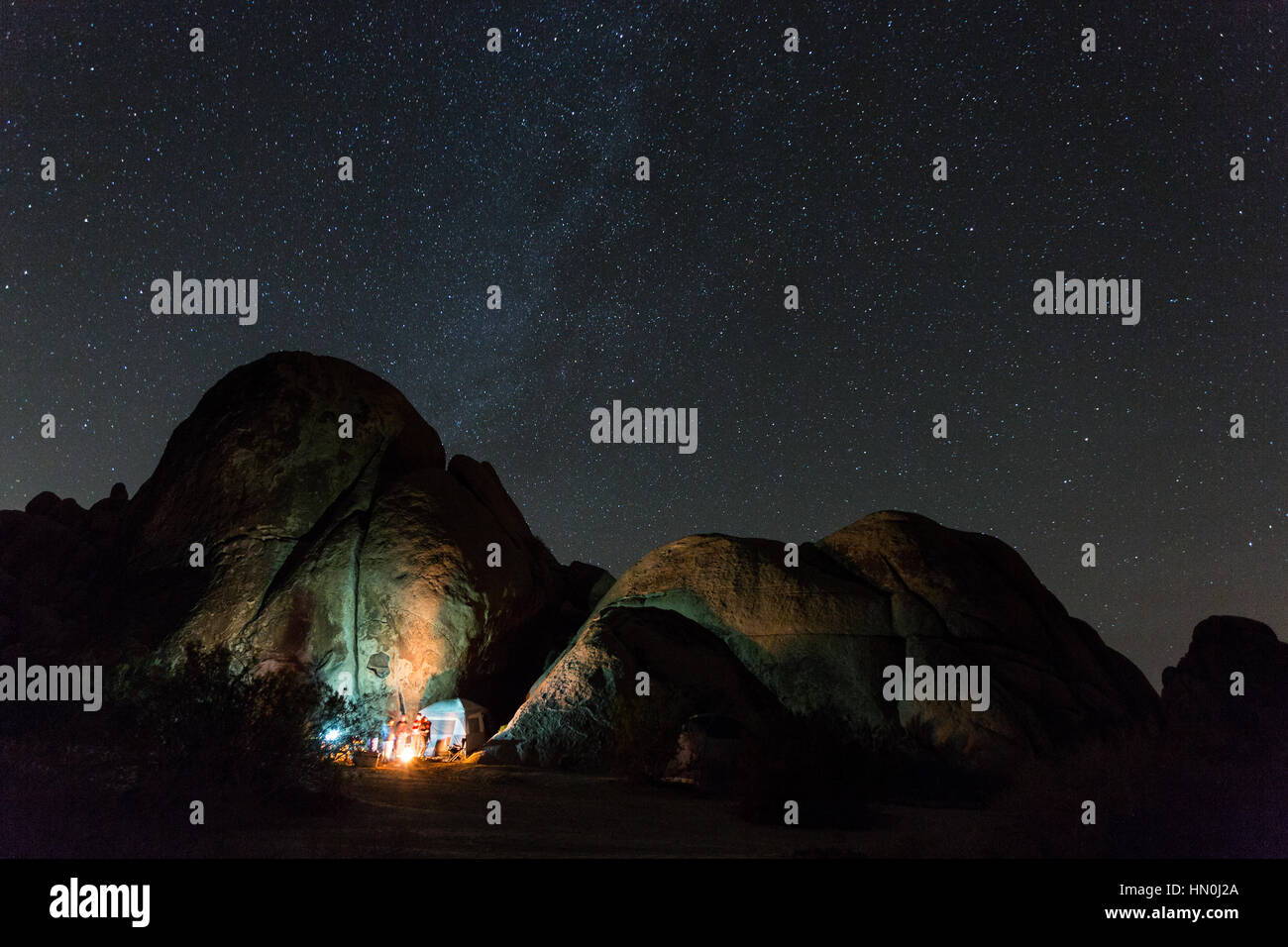 A campfire illuminates the rocks at Indian Cove Campground in Joshua Tree National Park with several stars overheads. Stock Photo