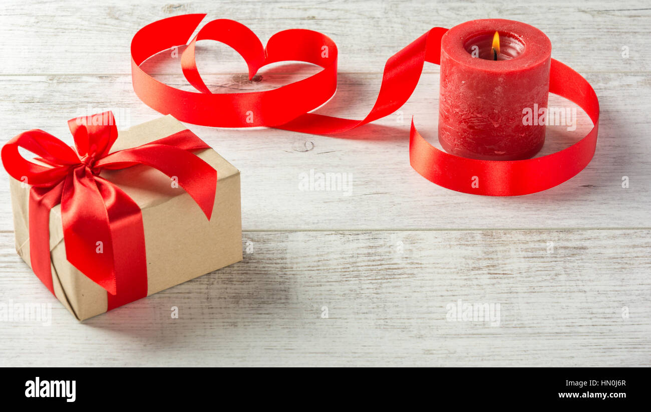 Box with a present to the Valentine's Day , red candle and tape on a white wooden table Stock Photo