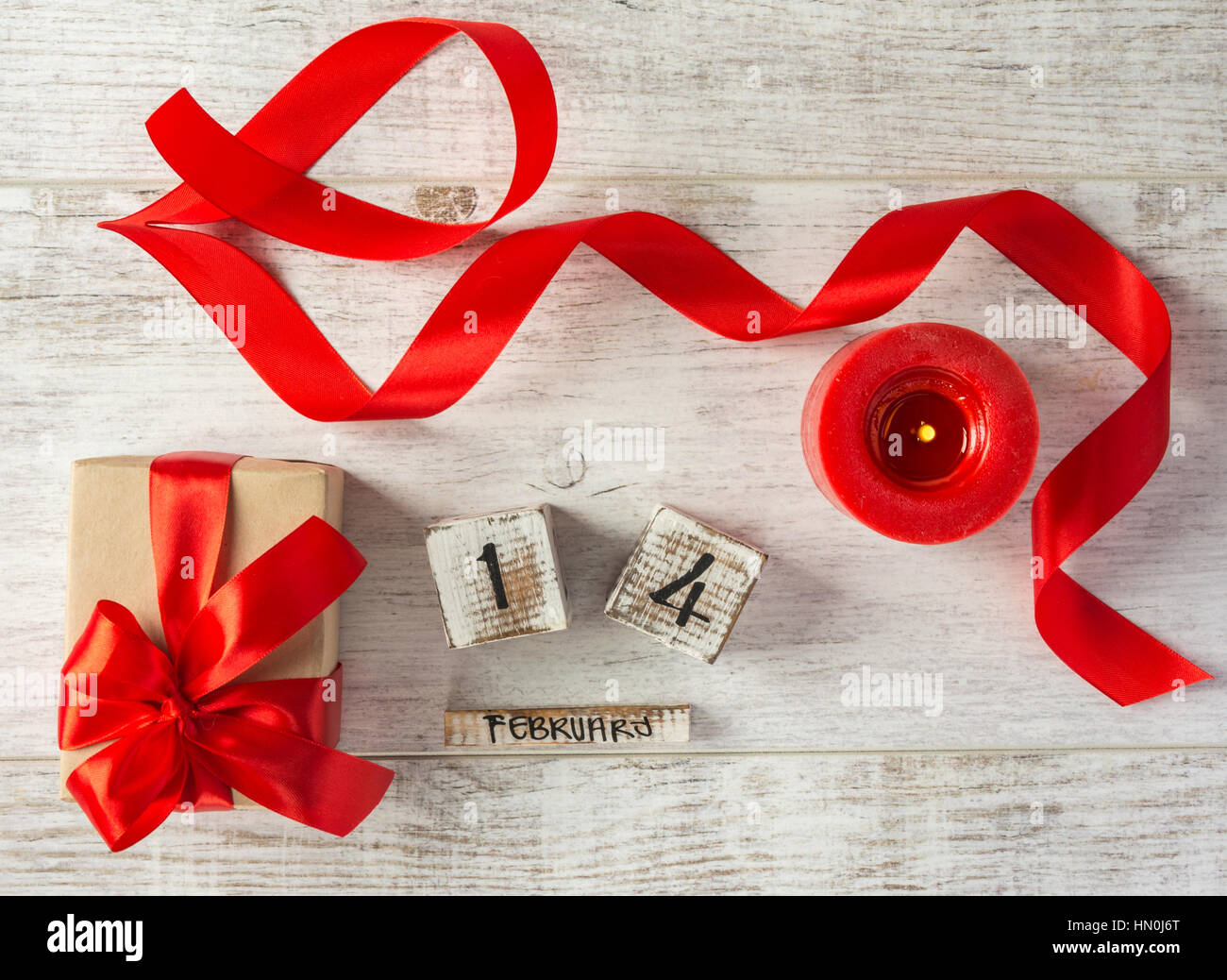 Box with a present to the Valentine's Day ,wooden calendar, red candle and tape on a white wooden table. Top view. Stock Photo