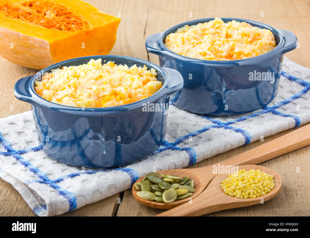 millet porridge with pumpkin in blue bowl on a kitchen towel, pumpkin seeds and millet in a wooden spoon and pumpkin on a wooden table Stock Photo