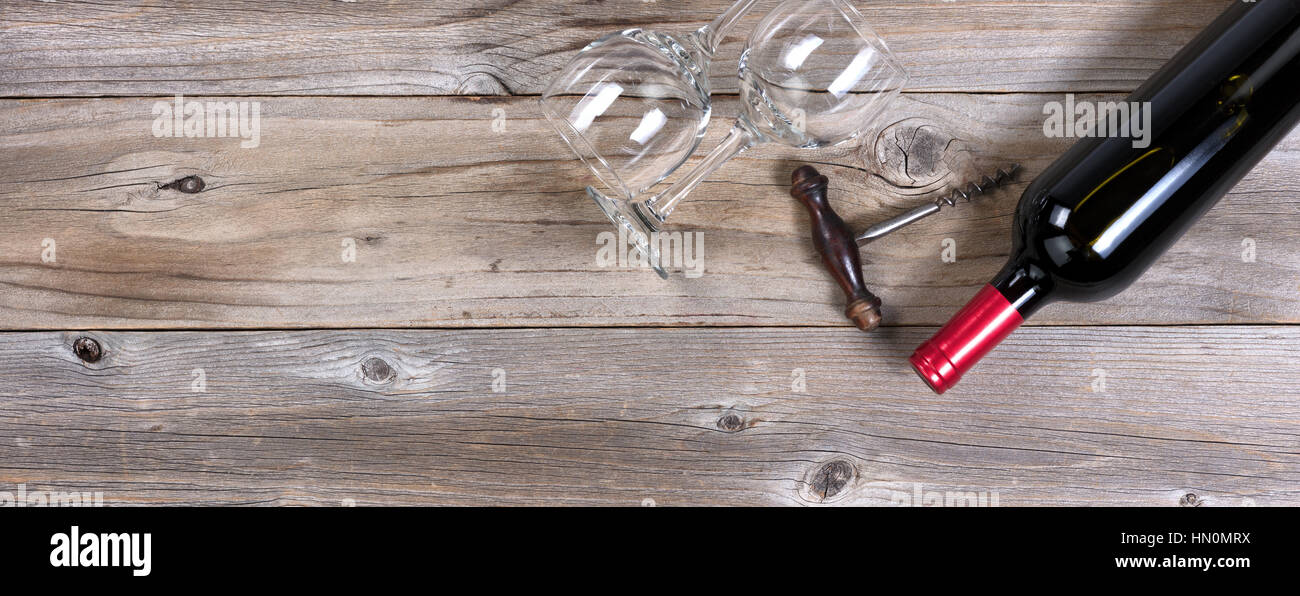 Flat view of a bottle of red wine, antique corkscrew, and drinking glasses on rustic wooden boards Stock Photo