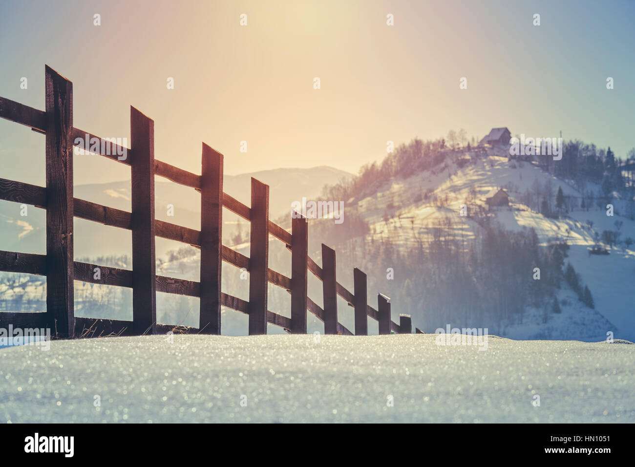 Beautiful countryside landscape with wooden fence and sunrise light over snow covered hills and valleys in Rucar-Bran pass, Romania. Selective focus. Stock Photo