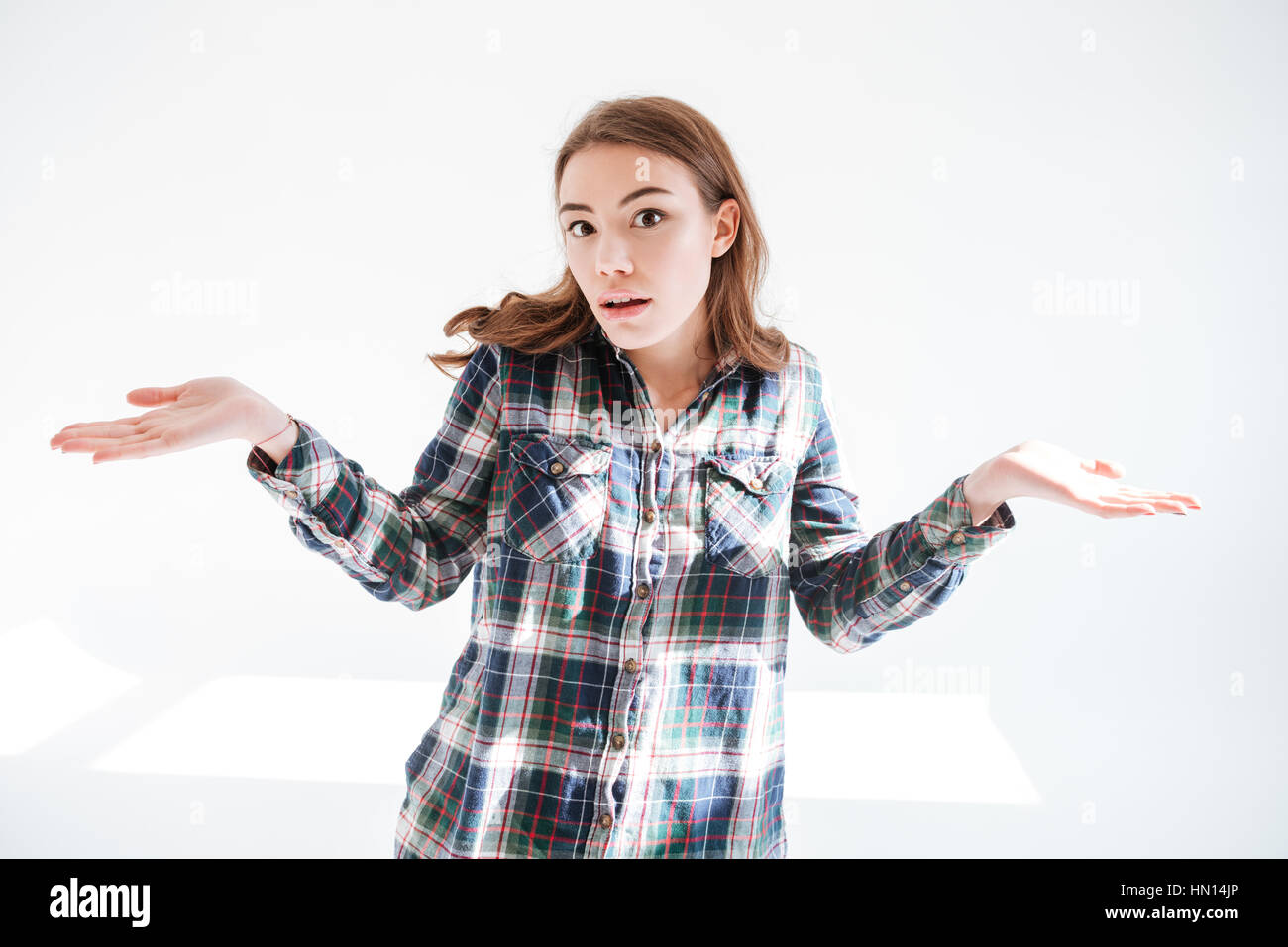 Confused pretty young woman shrugging shoulders and holding copyspace on both palms over white background Stock Photo