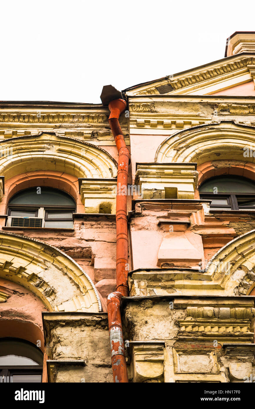 Details of an old building with deteriorated and dilapidated front face. Windows and orange painted heavily used rain pipe or water spout. Isolated Stock Photo
