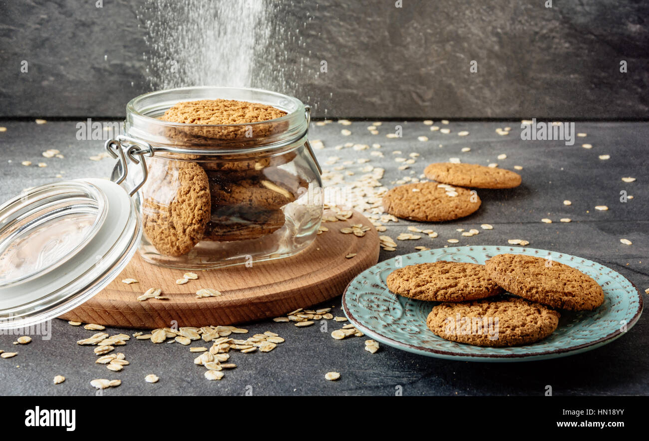 Oat cookies lay on a plate and bank with oatmeal cookies standing on a wooden board. Stock Photo