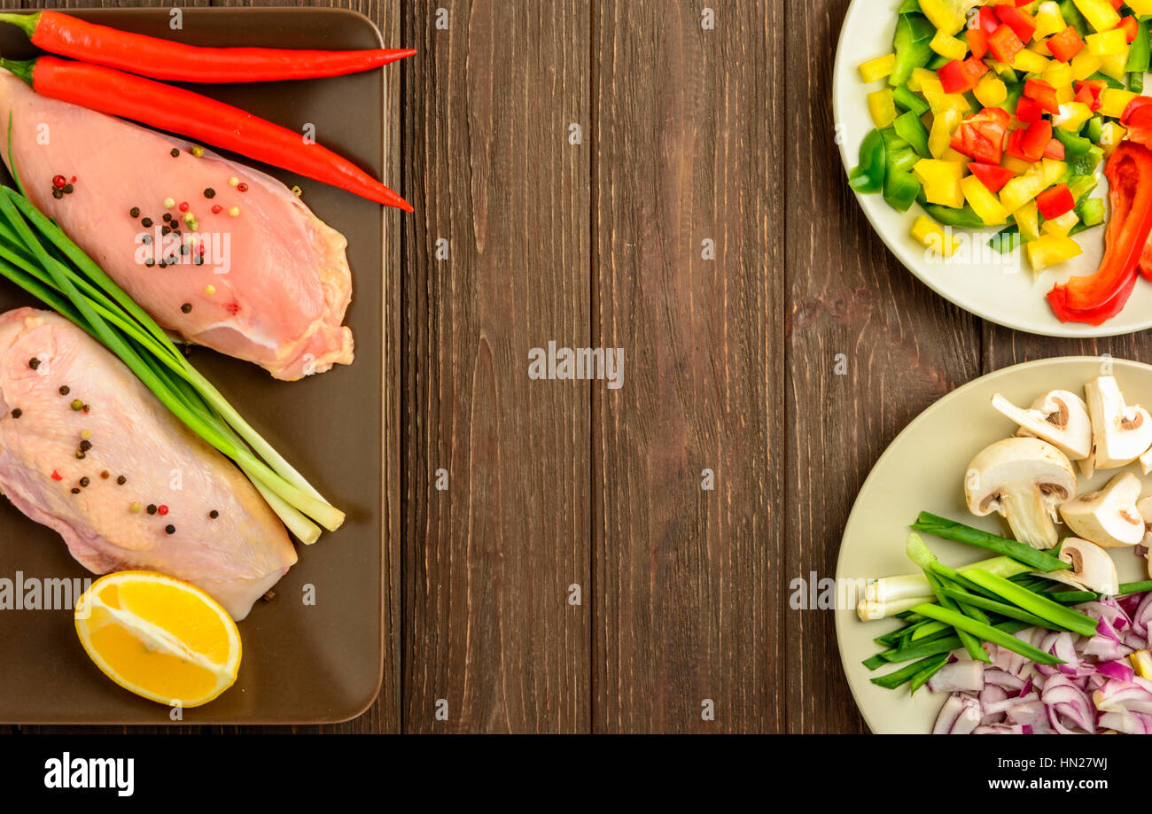 The chicken fillet and vegetables prepared for frying on a brown wooden background. Top view, copy space. Stock Photo