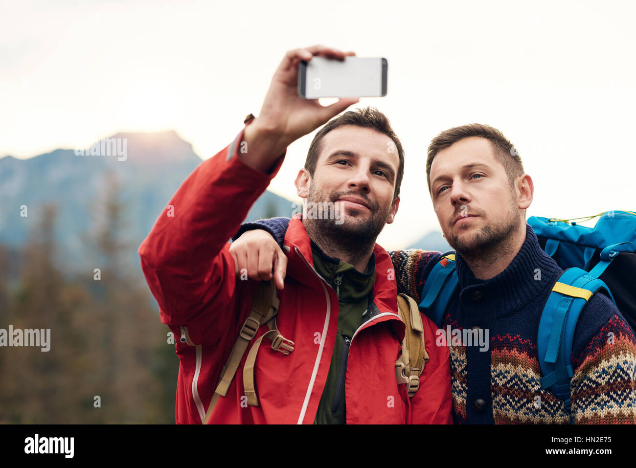 Two young men in hiking gear standing outside taking a selfie with ...