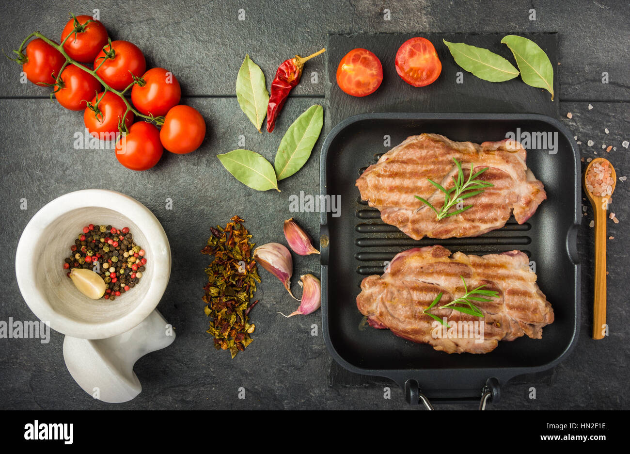 steak with spices and tomatoes cooked on the grill pan on a dark table top view Stock Photo